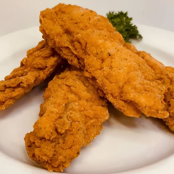 Crispy golden-brown chicken tenders on a white plate, garnished with a sprig of parsley.