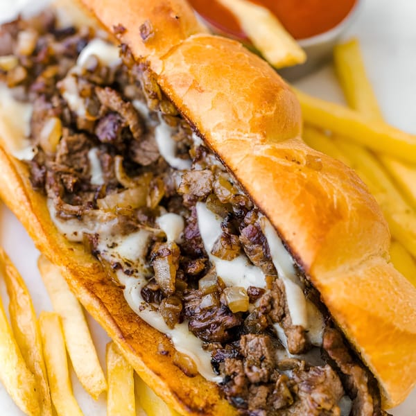 A Philly cheesesteak sandwich with melted cheese and onions, served with golden fries and ketchup.