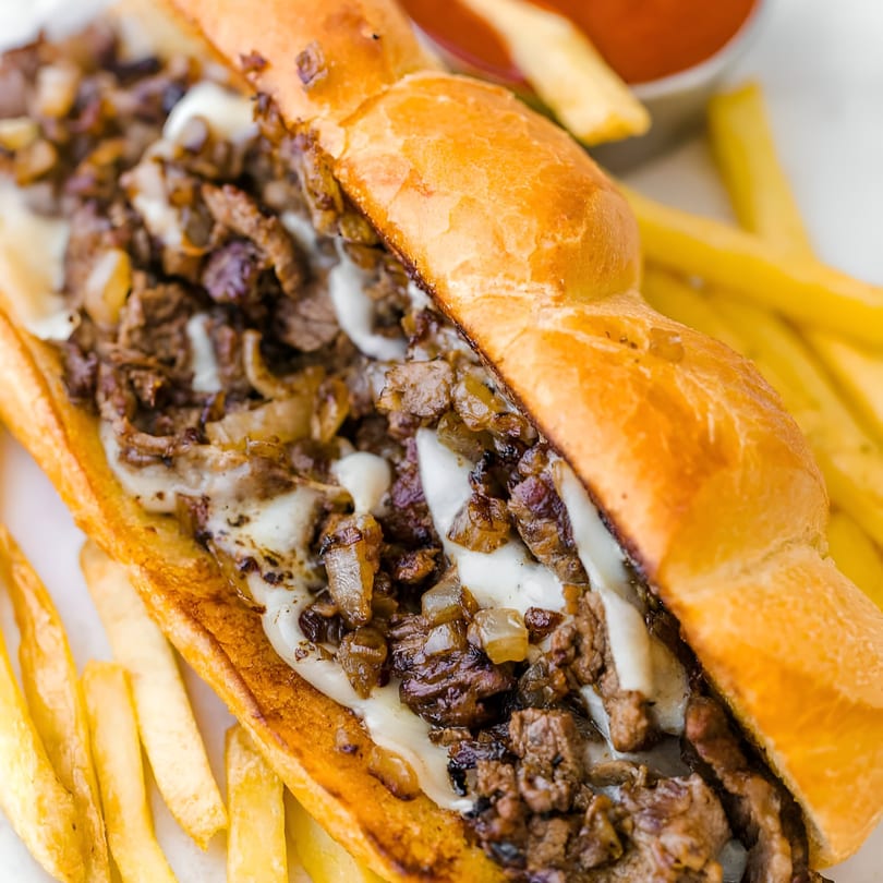 A Philly cheesesteak sandwich with melted cheese and onions, served with golden fries and ketchup.