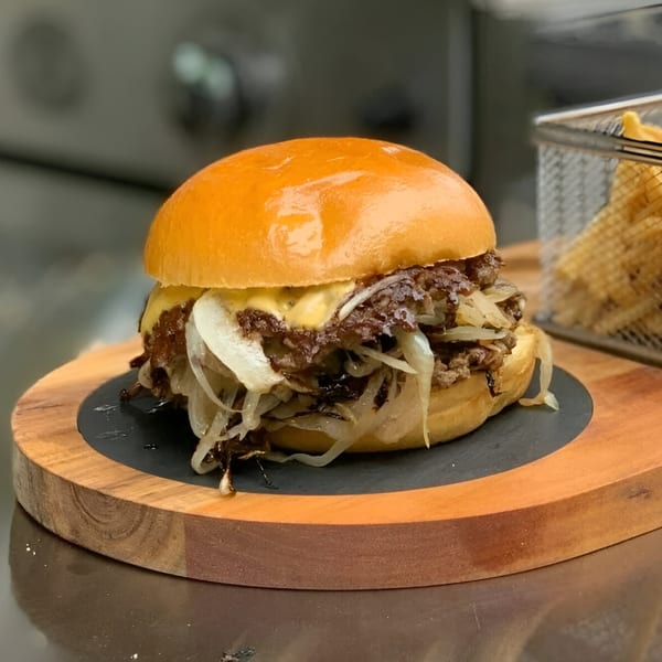 A A1 Smash Midtown burger with melted cheese and caramelized onions on a wooden board with fries.