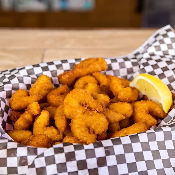 Golden fried shrimp in a checkered paper-lined basket with a lemon wedge.